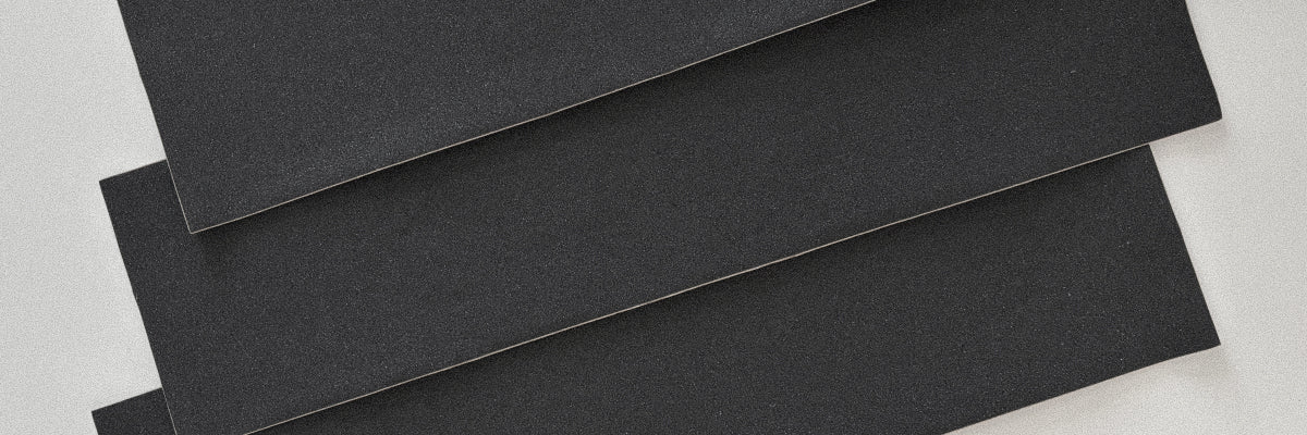Three overlapping black skateboard griptape sheets on a light gray background.